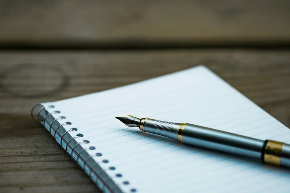 Carnet à spirale et stylo plume posés sur une table en bois sombre