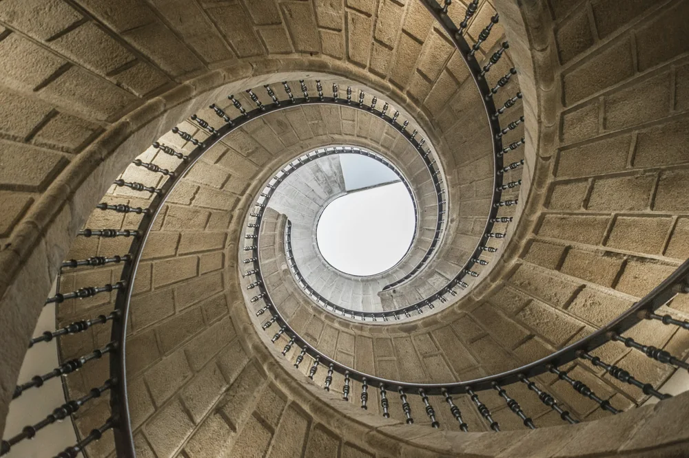 Escalier en spirale de pierre vu d'en bas, qui s'enroule vers une ouverture claire