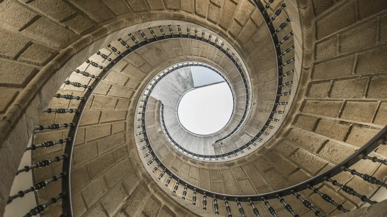 Escalier en spirale de pierre vu d'en bas, qui s'enroule vers une ouverture claire
