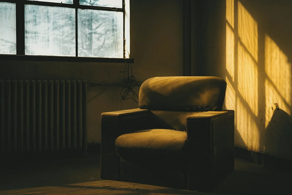 Fauteuil ocre près d'une fenêtre, lumière dorée de fin de journée