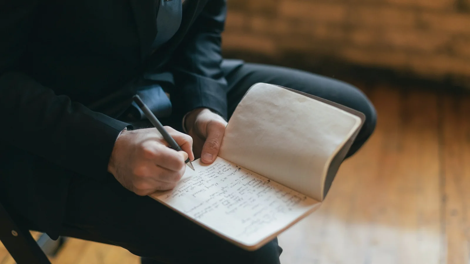 Personne assise de profil, sans visage visible, qui note à la main dans un carnet posé sur ses genoux