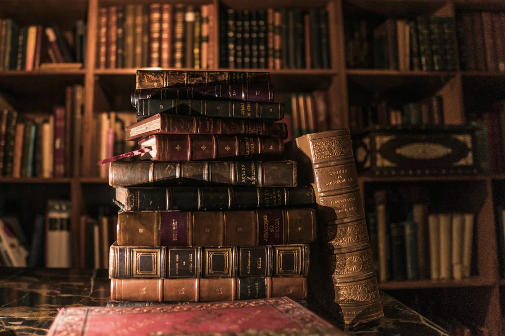 Pile de vieux livres reliés de cuir devant une bibliothèque