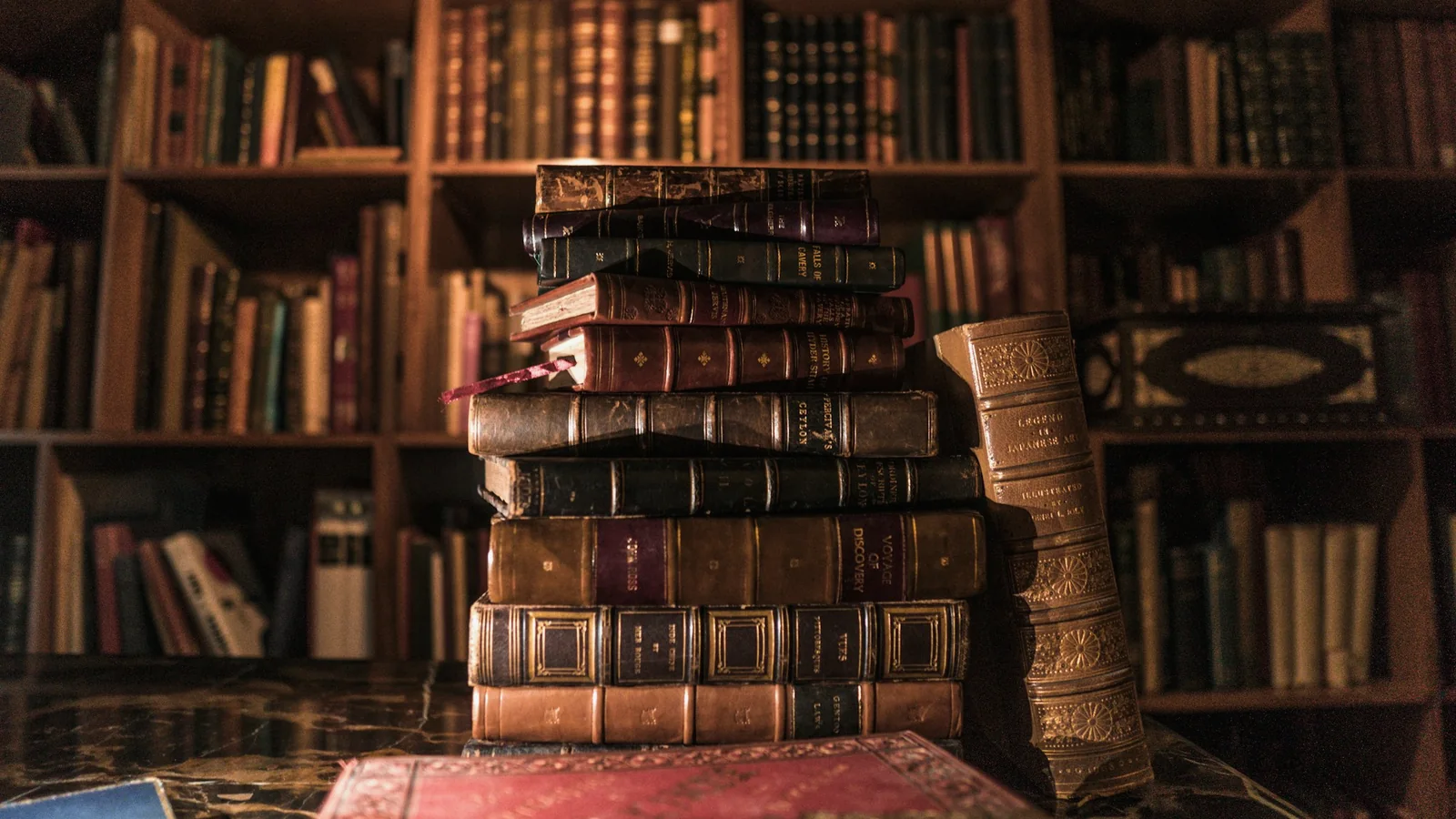 Pile de vieux livres reliés de cuir devant une bibliothèque