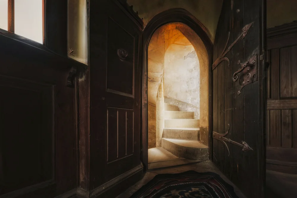 Porte ouverte en bois sombre sur un escalier en pierre baigné de lumière chaude