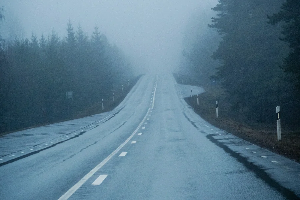Route sinueuse dans la brume bleutée, qui disparaît vers l'horizon
