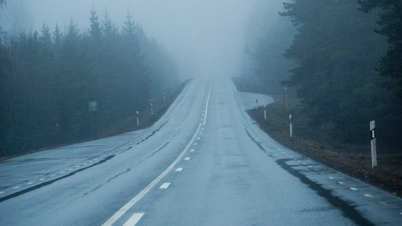 Route sinueuse dans la brume bleutée, qui disparaît vers l'horizon
